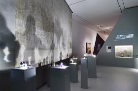 Ausstellungsraum mit Golem-Actionfiguren, die auf Sockeln stehen und Schatten an die Wand werfen