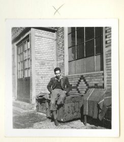 Ein junger Mann sitzt vor einem Haus (Schwarz-Weiß-Foto)