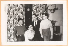 Auf dem schwarz-weiß Foto ist die Familie in einem Interieur der gemusterten Vorhängen und Zimmerpflanzen zu sehen. Alle vier lachen oder lächeln. Das Bild wirkt bewegt.