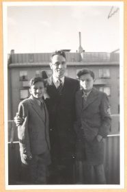 Auf dem schwarz-weiß Foto steht Rolf Rothschild steht in der Mitte und hat seine Arme um die beiden Jungen gelegt. Alle tragen Anzug.