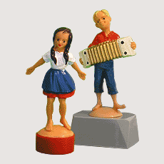 Zwei Plastikfiguren: Junge mit Ziehharmonika und Mdchen, das sich im Kreis dreht.