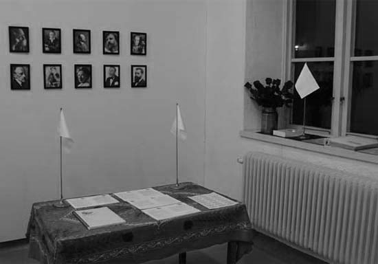 View of a room with a table, flags, portraits and a window.