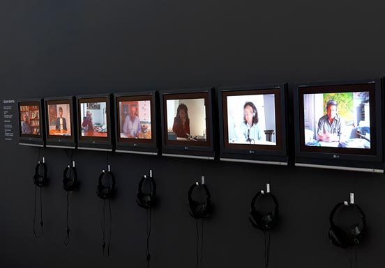 seven monitors with headphones along a wall