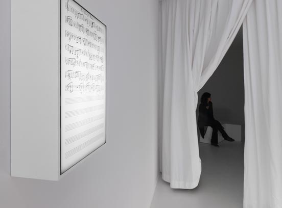 Leuchtkasten mit Notenschrift an der Wand und Einblick in einen Raum hinter einem Vorhang