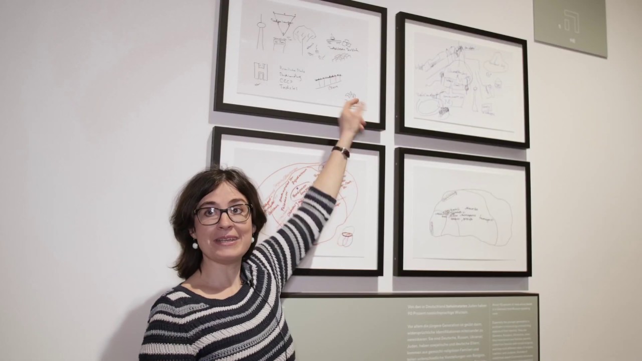 Woman with glasses pointing at pictures in an exhibition.