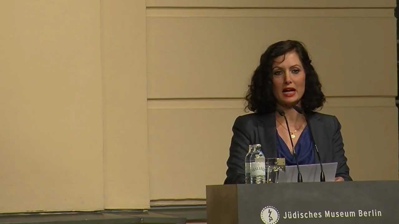 Eine Frau auf einer Bühne hinter einem Pult hält eine Rede.