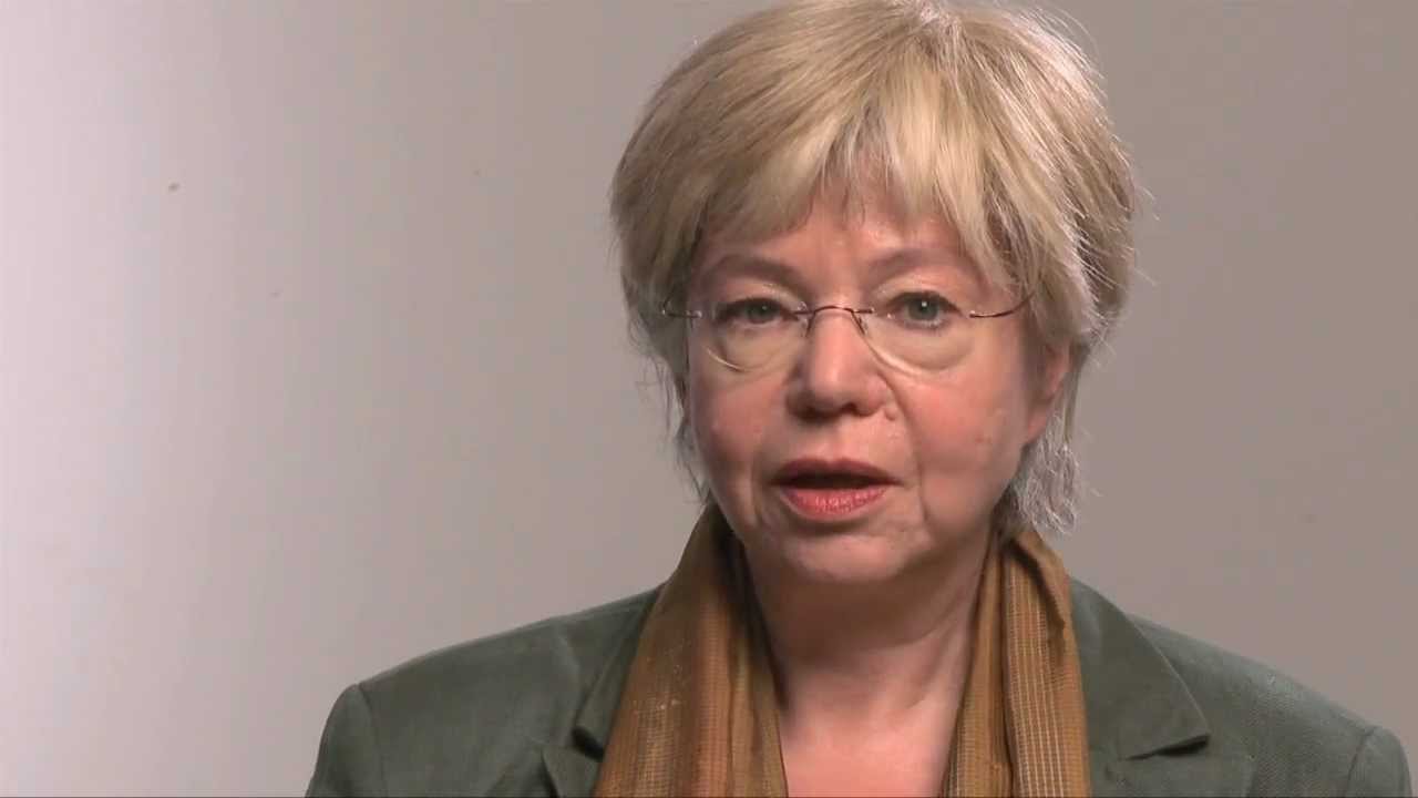 Woman with short blond hair and glasses speaks into the camera.