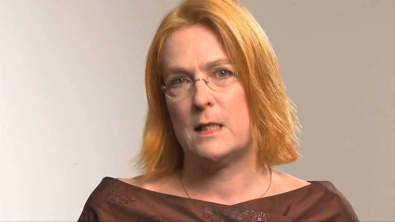 Woman with reddish hair and glasses speaks into the camera.