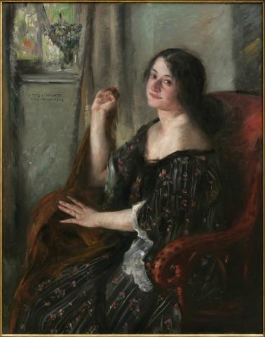 Porträt einer Frau (Charlotte Berend), die im Dreiviertelprofil auf einem roten Sessel vor einem Fenster sitzt.