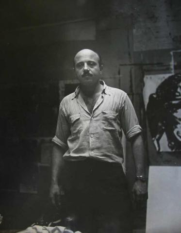 Black and white portrait of Boris Lurie standing in his studio 