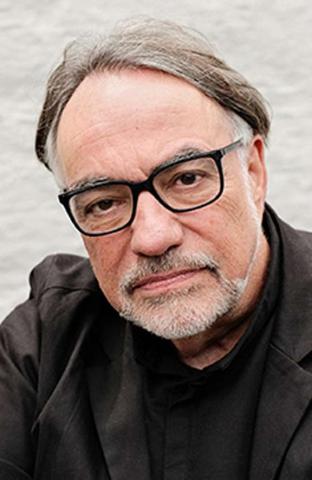A man with a gray beard and glasses in a brown jacket.