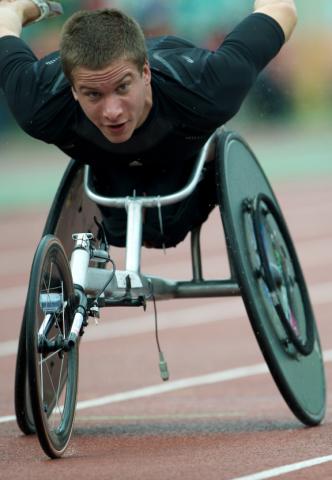 A racing wheelchair rider in a black jersey rides on a racetrack.