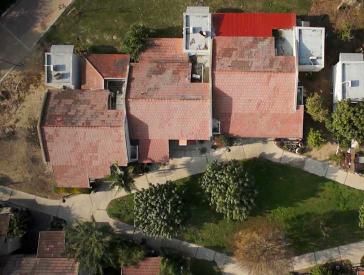 Bird’s eye view of several row houses with red roofs. They are surrounded by trees, front gardens and driveways.