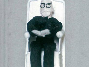 A small cloth figurine of a sitting man with a white beard and glasses.