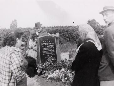 Black and white photograph of people at a grave with flowers.