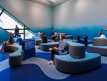 Raum in Blautönen mit wellenförmigen Sitzgelegenheiten und eingelassenen Fernsehbildschirmen