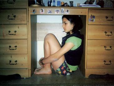 Girl in shorts crouches under a desk