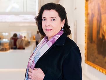 The color photograph shows Elena Bashkirova in a black blazer and a violet patterned scarf. In the background is the Jerusalem exhibition.