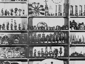 Black and white photograph of a shelf filled with Hanukkah candelabras.