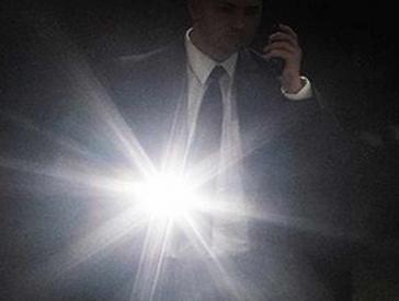 Man in suit holding a brightly lit flashlight.