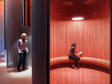 Exhibition view: one visitor stands under a sound tube, another sits in a sound bunk