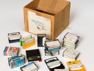 Empty cardboard box with a white label. A dozen music cassettes lie around it.
