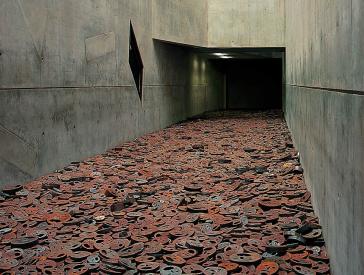 Menashe Kadishmans Installation: zahlreiche Eisenplatten, in die Gesichter geschnitten sind, liegen auf dem Boden eines Voids.