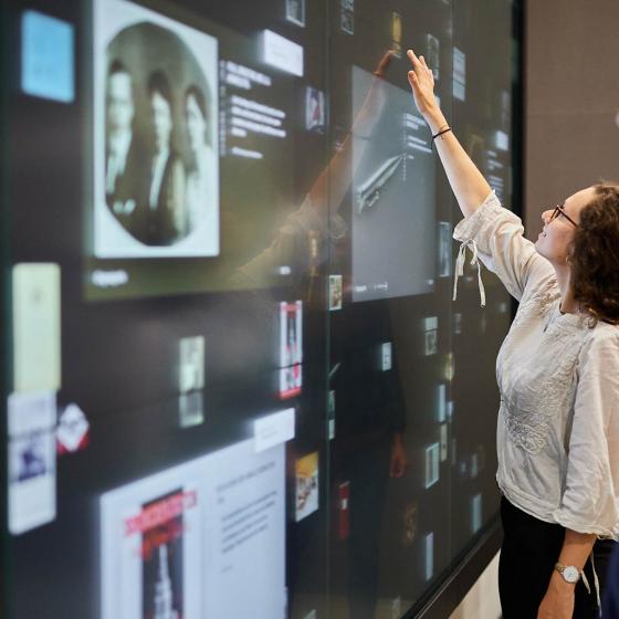 Person berührt eine interaktive Wand mit digitalen Objekten und Dokumenten