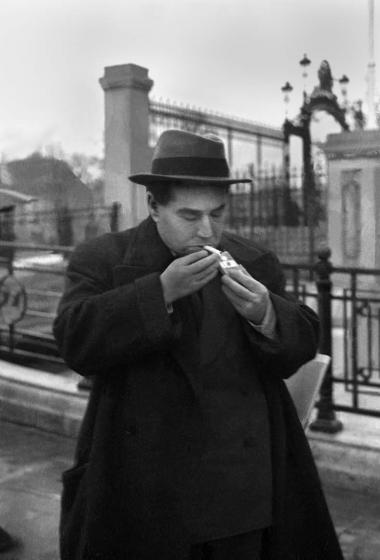 Black-and-white portrait of Egon Erwin Kisch, who is lighting a cigarette on the street