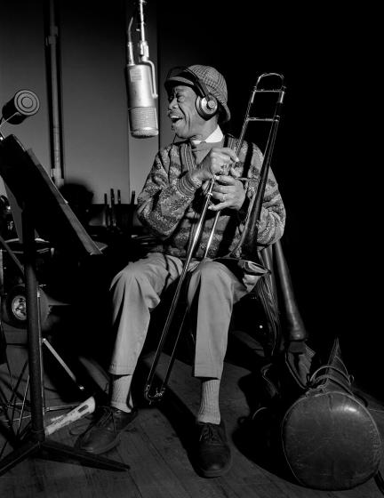 Al Grey sitzt mit Posaune in der Hand im Aufnahmestudio und singt in ein vor ihm hängendes Mikrofon. 
