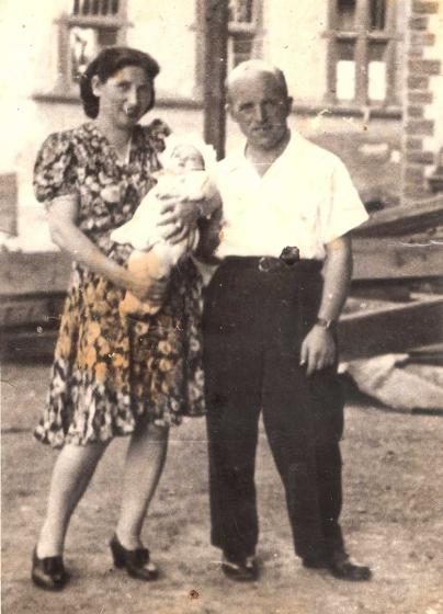 Black and white photo of a woman holding an infant and standing beside a man