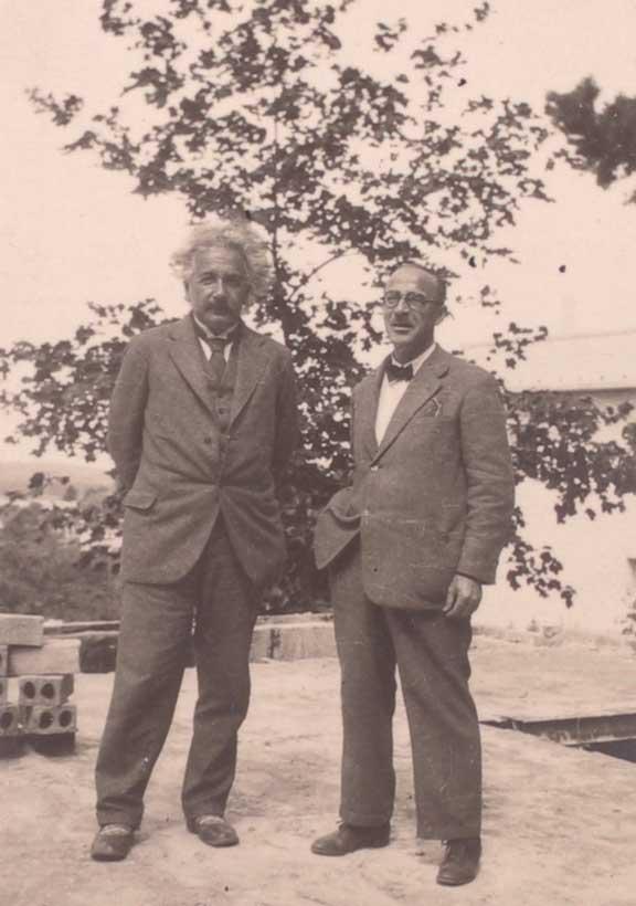 Black and white photograph of two middle aged men in suits standing in front of a tree.