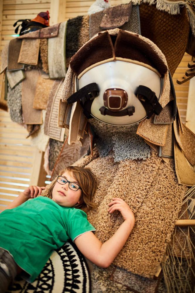 Boy lies on a sloth made of carpets and looks into the camera
