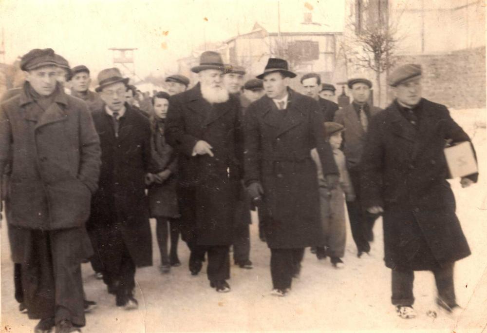 Black and white photo of a larger group of people in coats and hats walking towards the viewer