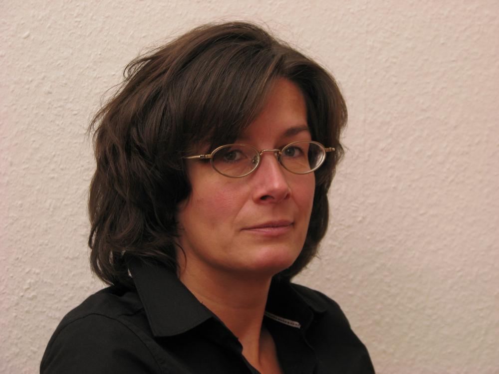 Portrait of Karen Körber, she has dark hair, and is wearing oval glasses