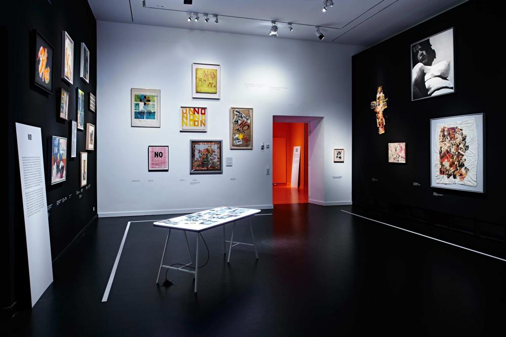 A black and white exhibition space with pictures on the walls and a table with photos in the middle.