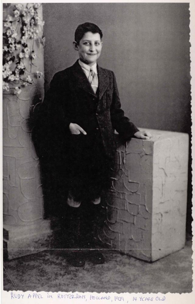 Portrait of Rudolf Appel standing in a photo studio. He is wearing a dark suit with short trousers and knee-high socks.