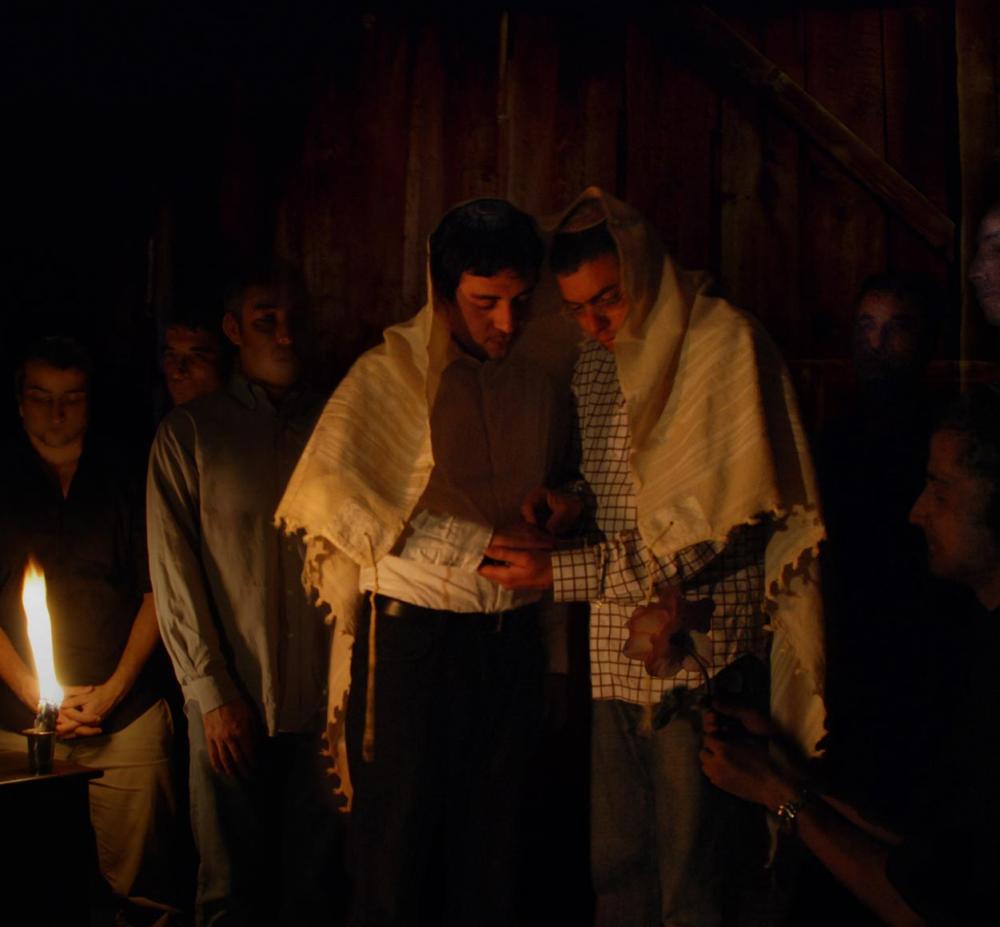 Zwei Männer in der Pose ikonischer jüdische Hochzeitszeremonien, einer streift dem anderen einen Ring über.