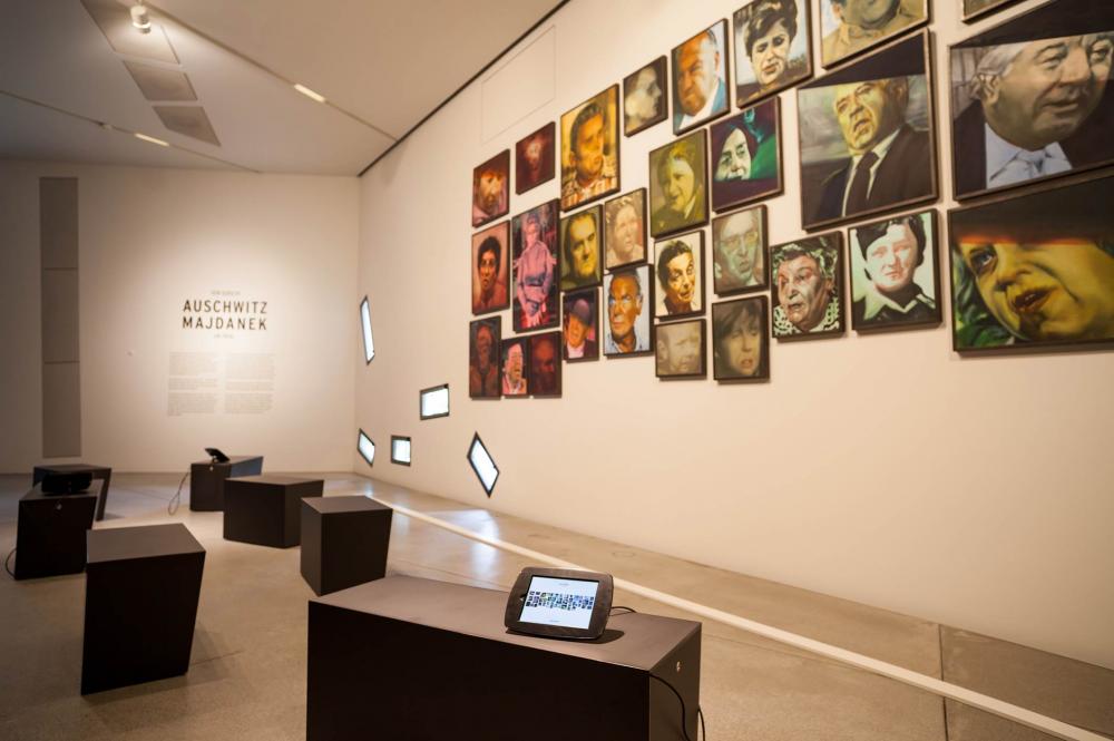 An den Wänden hängen bunt bemalte Porträts von Männern und Frauen vor schwarzen Stühlen mit Tablets.