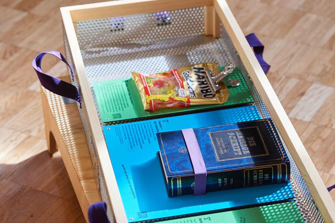 In einer Kiste aus Blech und Holz liegt eine Packung Gummibärchen und ein dickes Buch.