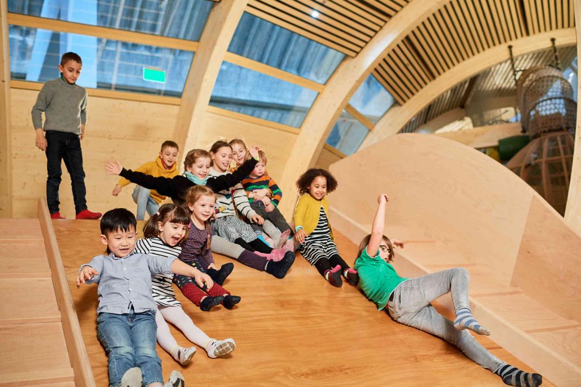 11 children slide down a wide wooden slide