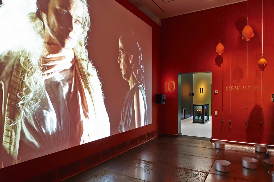 A red room with one wall covered by a giant projector screen, the screen is showing an image of two women
