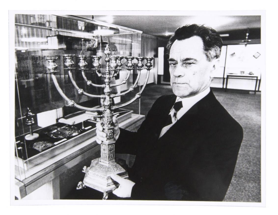 Black and white photo of man in suit with big hanukkah menorah in hand