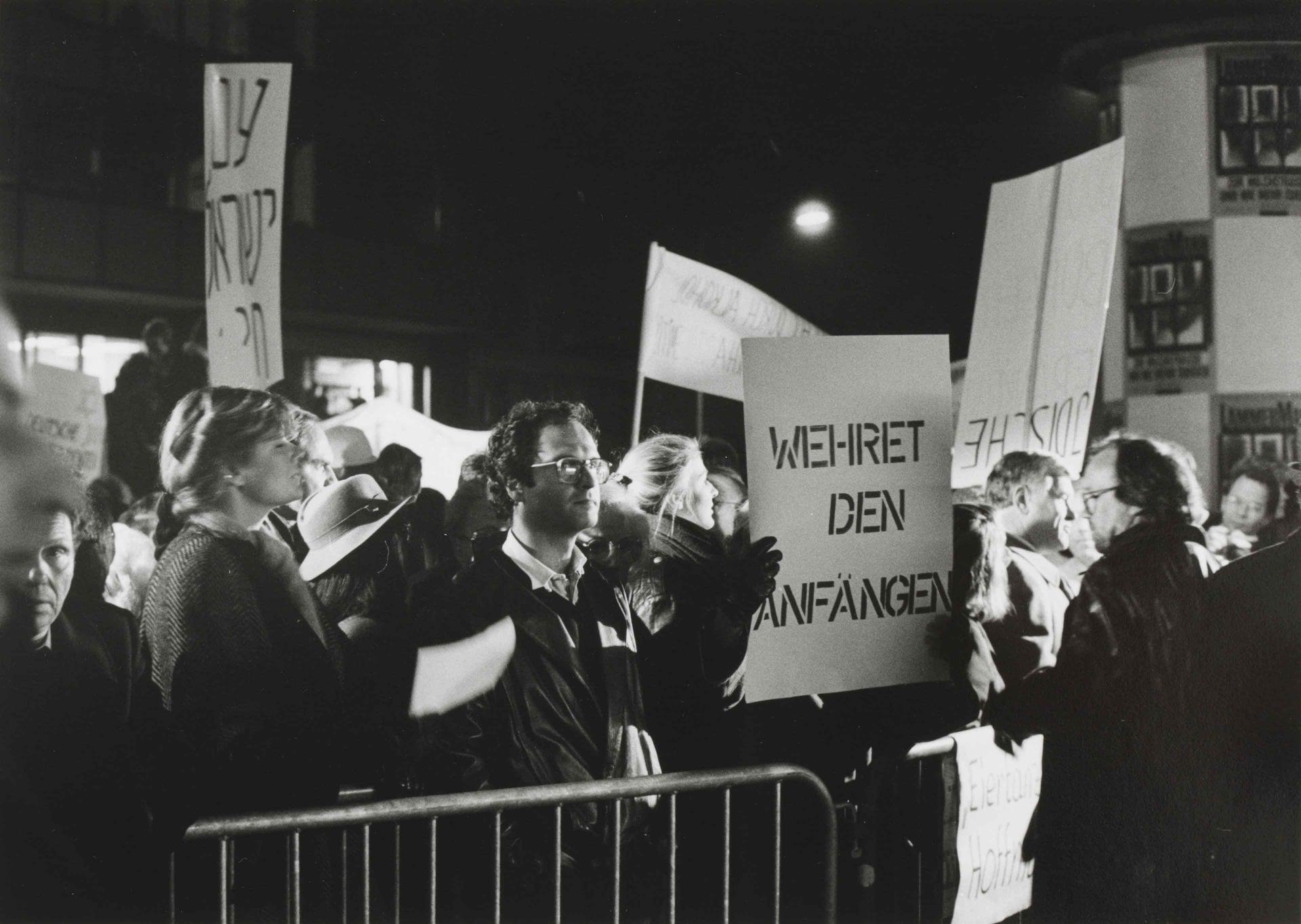 Black-and-white photograph of protesters with placards bearing slogans such as "Resist the beginnings".