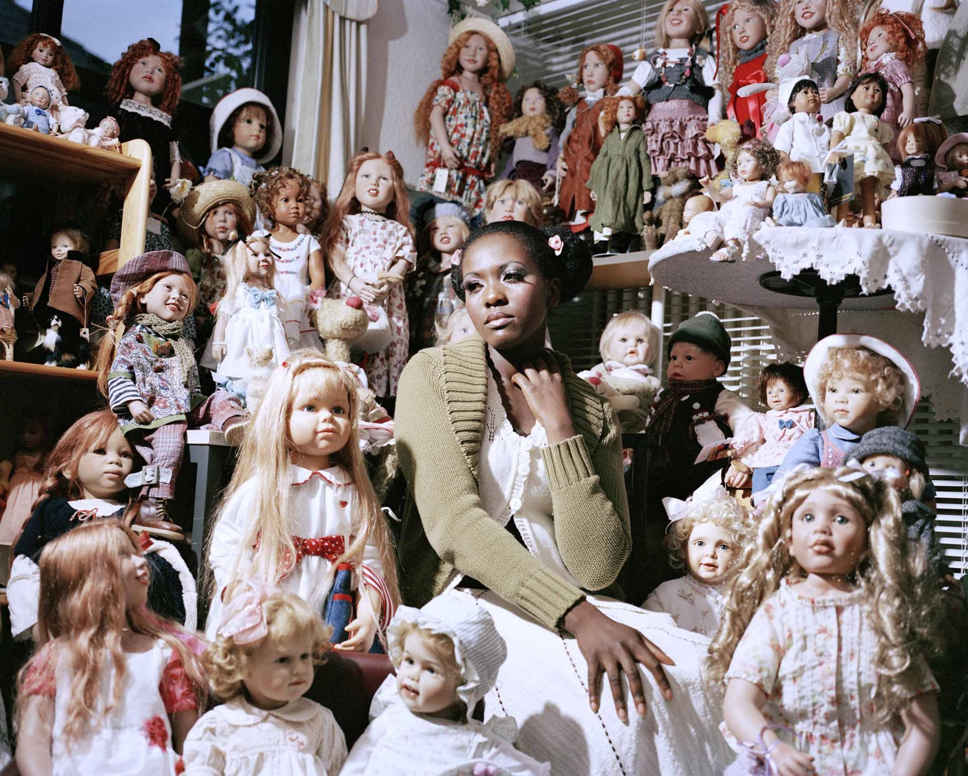 Young black woman in white dress surrounded by countless white dolls