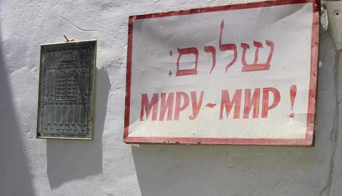 Hauswand mit einem Schild, auf dem in hebräischen Buchstaben Shalom und auf Russisch Friede für die Welt steht