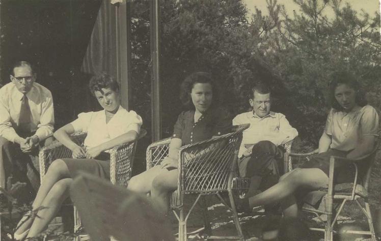 Schwarz-weiß Fotografie von zwei Männern und drei Frauen, die auf Stühlen in einem Garten sitzen.