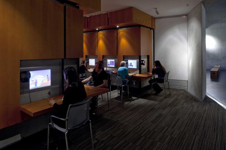 Interior view of the Rafael Roth Learning Center in the basement of the Jewish Museum Berlin. Several people are looking at screens.