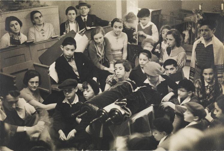 Black-and-white photograph showing children and teenagers at a festive prayer service in a synagogue