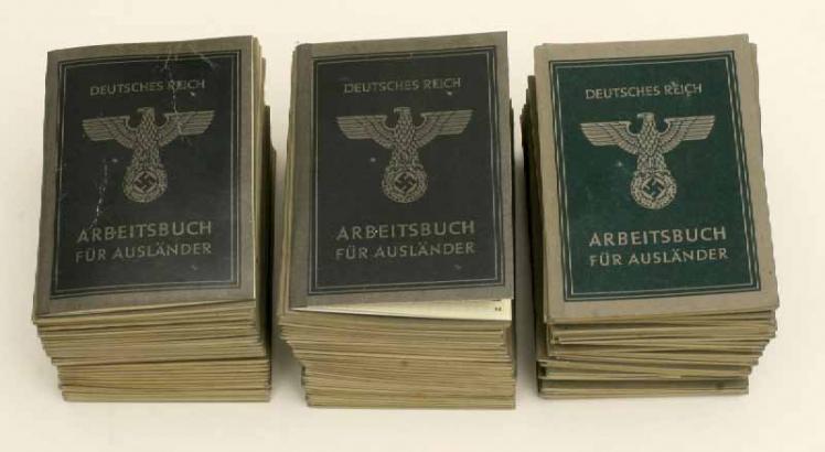 Drei Stapel Arbeitsbücher mit Reichsadler, Hakenkreuz und der Beschriftung „Deutsches Reich, Arbeitsbuch für Ausländer“